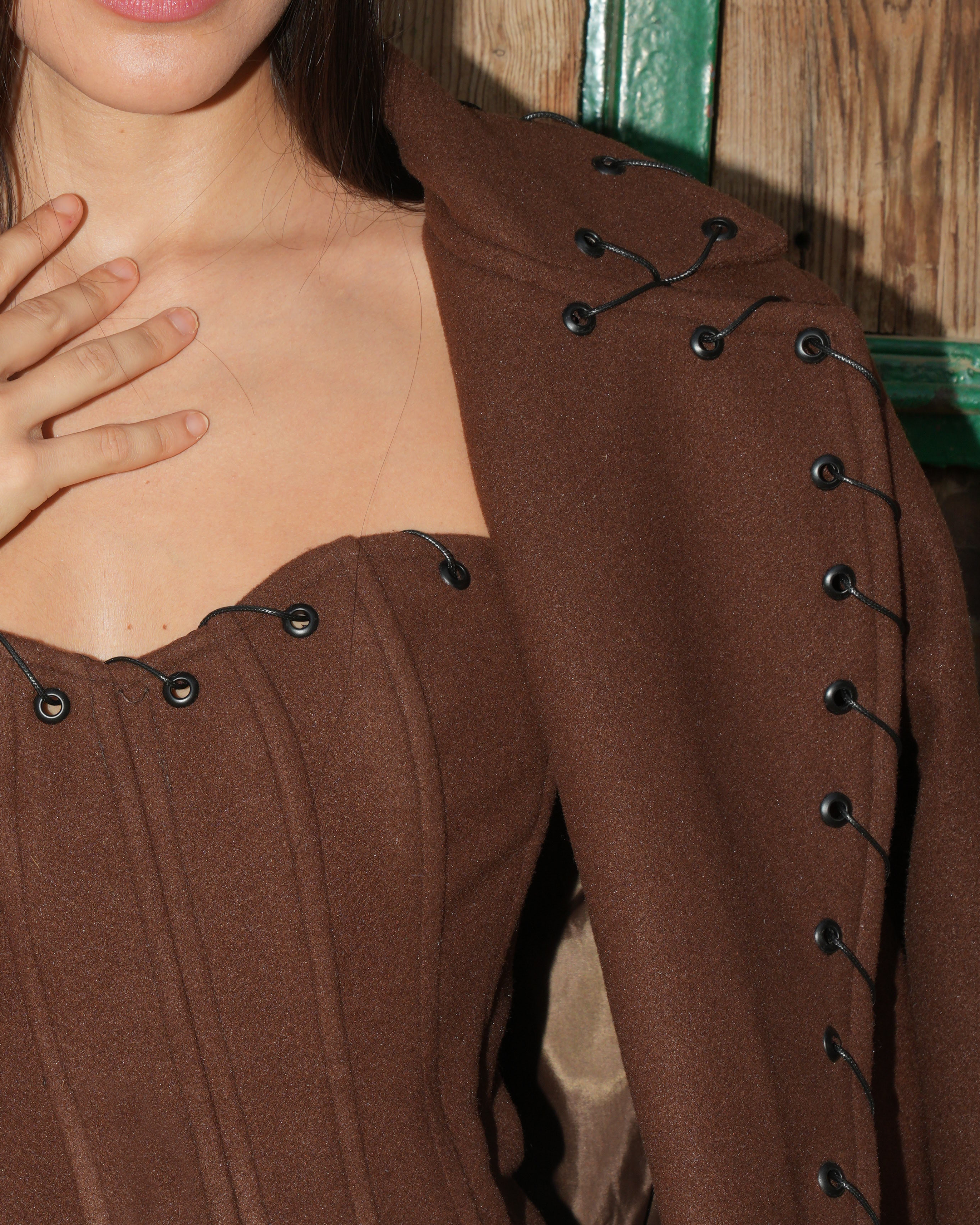 Close-up detail of a brown textured Western-style corset top featuring black lace-up grommets on the bodice and shoulder.