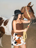 Model wearing Baloska brown corset top and faux fur cow print mini skirt posing with a horse
