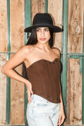 Woman wearing a brown strapless top and black hat against a wooden background